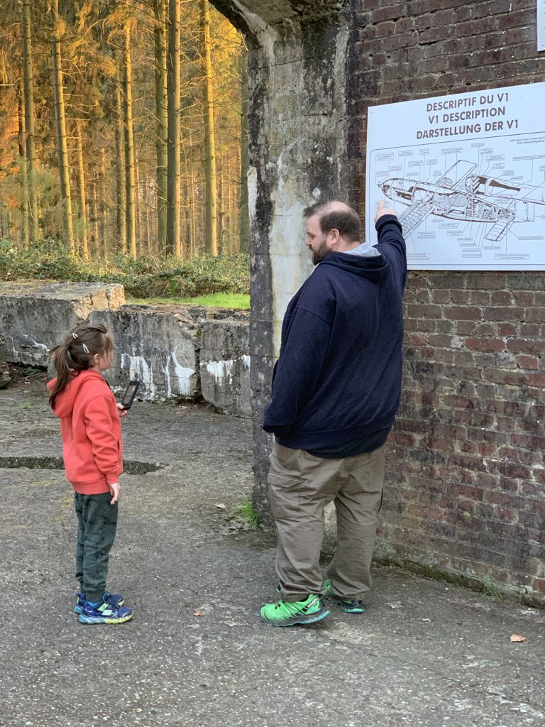 George points to a cutaway drawing of a V1 while Olivia looks on